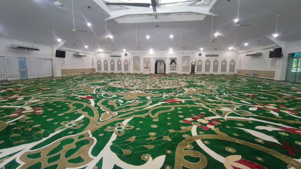 Pemandangan sudut pandang luas ruang dewan solat utama memaparkan hasil siap pemasangan karpet masjid custom-made gred premium berwarna hijau tua dengan corak flora suluran daun dan bunga medallion gergasi berwarna krim keemasan di Masjid Abu Bakar As-Siddiq SS19, Subang Jaya, Selangor, menunjukkan deretan panel mihrab putih di bahagian dinding depan tengah, kipas siling gantung, serta sistem pencahayaan lampu LED yang terang.