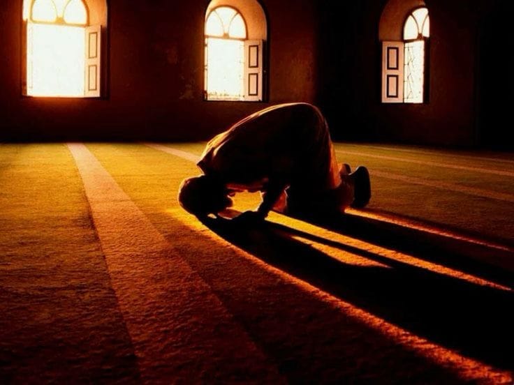 Kelibat siluet seorang lelaki sedang khusyuk bersujud menunaikan solat di dalam masjid dengan sinaran cahaya matahari pagi