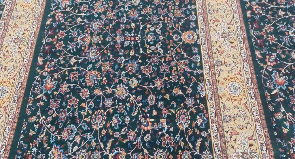 Pandangan dekat karpet hijau tua dengan corak bunga merah, biru dan krim serta jalur sempadan krim keemasan