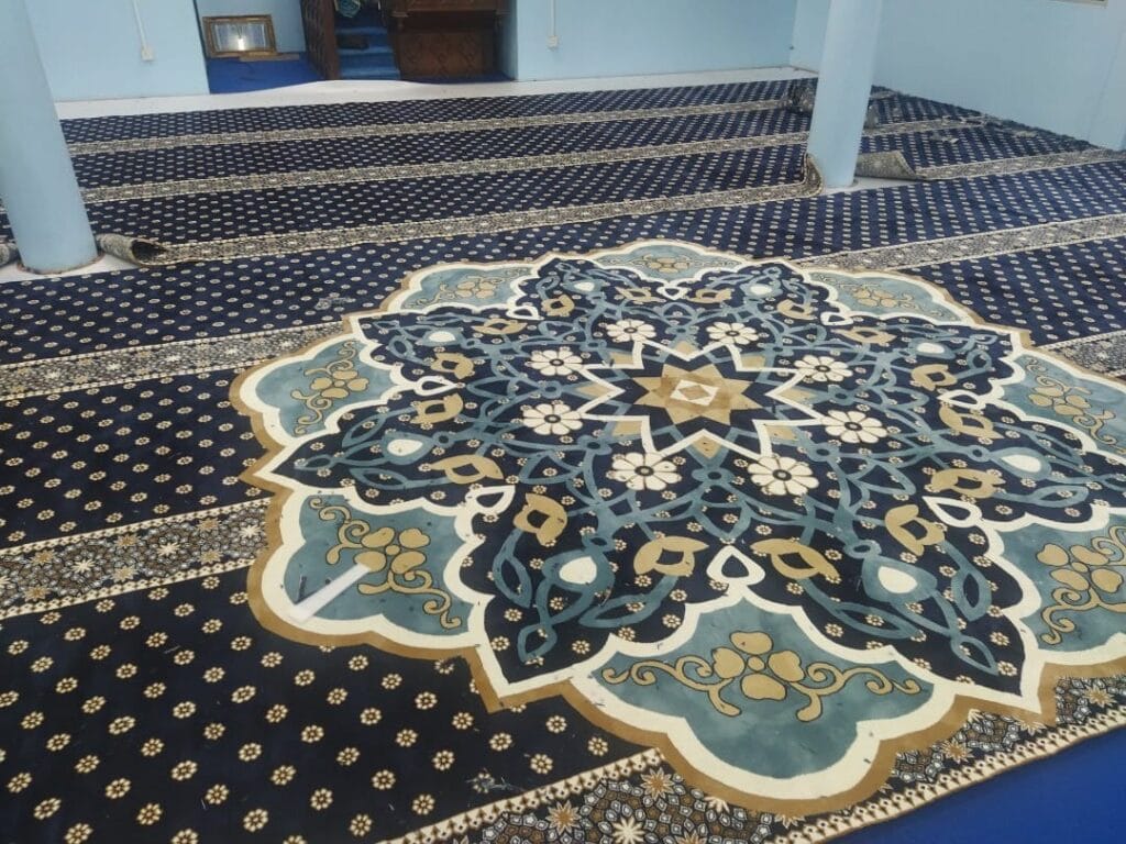 Pandangan dekat corak medallion hiasan tengah geometri Islamik pada karpet premium biru tua di Masjid Jamek Kg Acheh Pekan