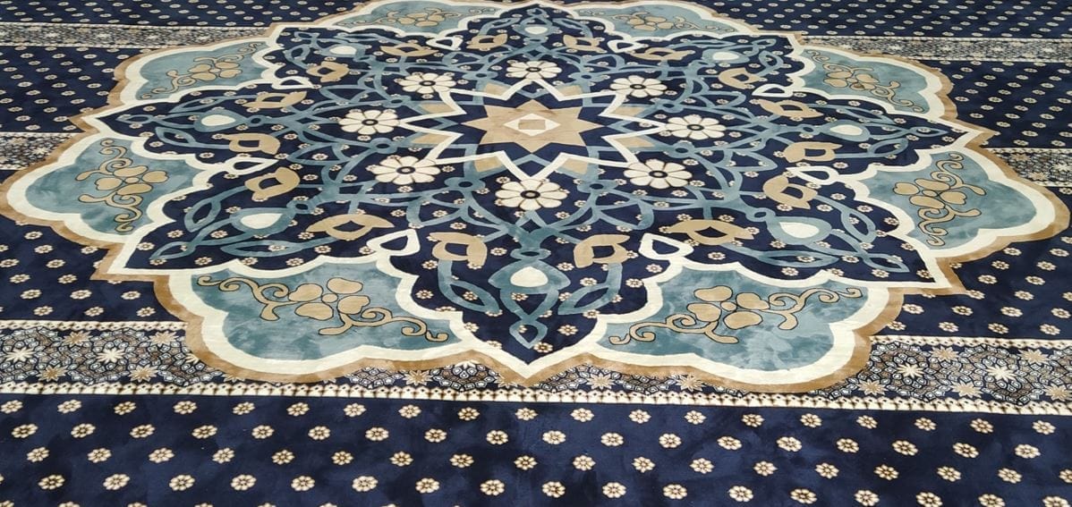 Keratan imej fokus corak hiasan tengah medallion geometri Islamik berwarna biru lembut dan emas pada karpet masjid gred premium