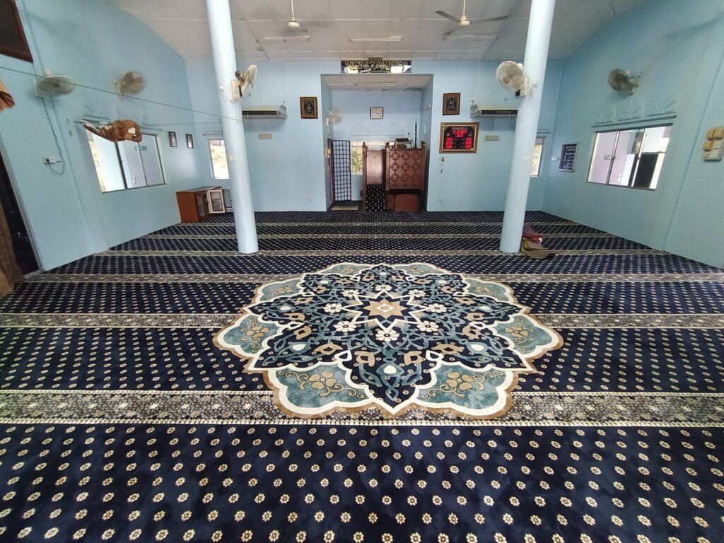 Pandangan luas dewan solat Masjid Jamek Kg Acheh Pekan menampilkan hamparan karpet premium biru tua dengan corak medallion tengah yang eksklusif