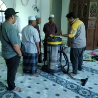 Gambar foto dokumentasi di dalam ruang solat utama memaparkan seorang wakil teknikal Nusantara Carpet memakai jaket seragam korporat kelabu kuning sedang berdiri memberikan penerangan sambil menunjuk ke arah satu unit mesin vakum industri silinder keluli besar berkepala kuning hitam bertayar roda, di hadapan barisan ahli jawatankuasa kariah masjid yang memakai baju melayu, jubah, kopiah putih, dan kain sarung, manakala di sebelah kiri kelihatan seorang kakitangan teknikal syarikat berseluar panjang hitam memakai topi sedang berdiri memerhatikan sesi taklimat di atas hamparan karpet masjid tebal premium warna kelabu kebiruan bercorak motif medallion lingkaran bunga saf lurus dengan latar belakang struktur mimbar kayu coklat tua di bahagian kanan